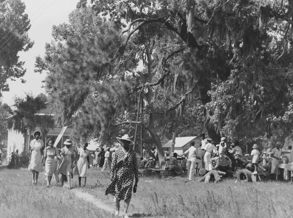 #23 A group of African American men and women, enjoying themselves at a picnic or garden party; with a woman, wearing a large hat and a polka-dotted dress at party, 1939