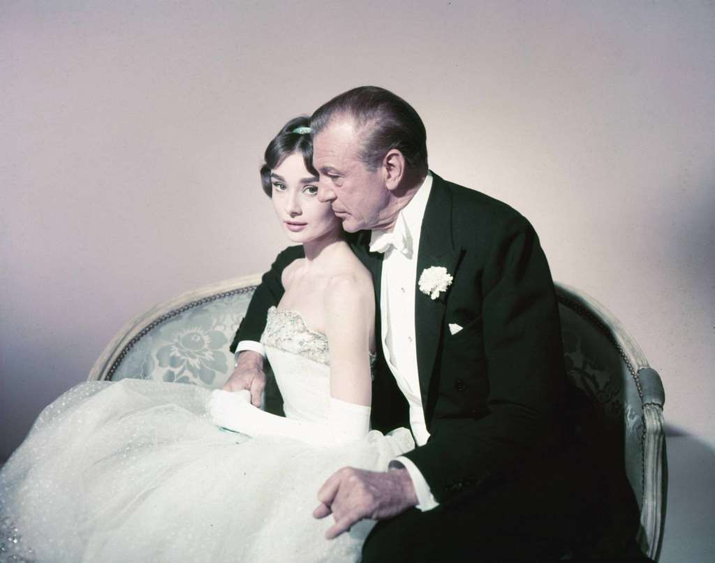 Audrey Hepburn wearing a strapless white dress, and Gary Cooper , wearing a black dinner jacket, white shirt with wing-top collars and a white bow tie, ‘Love in the Afternoon’, 1957.