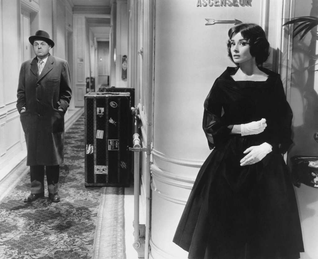 Ariane Chavasse (Audrey Hepburn) hides around a hallway corner from Monsieur X (John McGiver in a scene, ‘Love in the Afternoon’, 1957.
