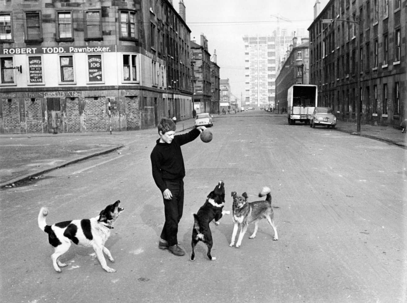 #101 A boy playing with dogs in a road of tenement housing in the Gorbals area of Glasgow, 1960