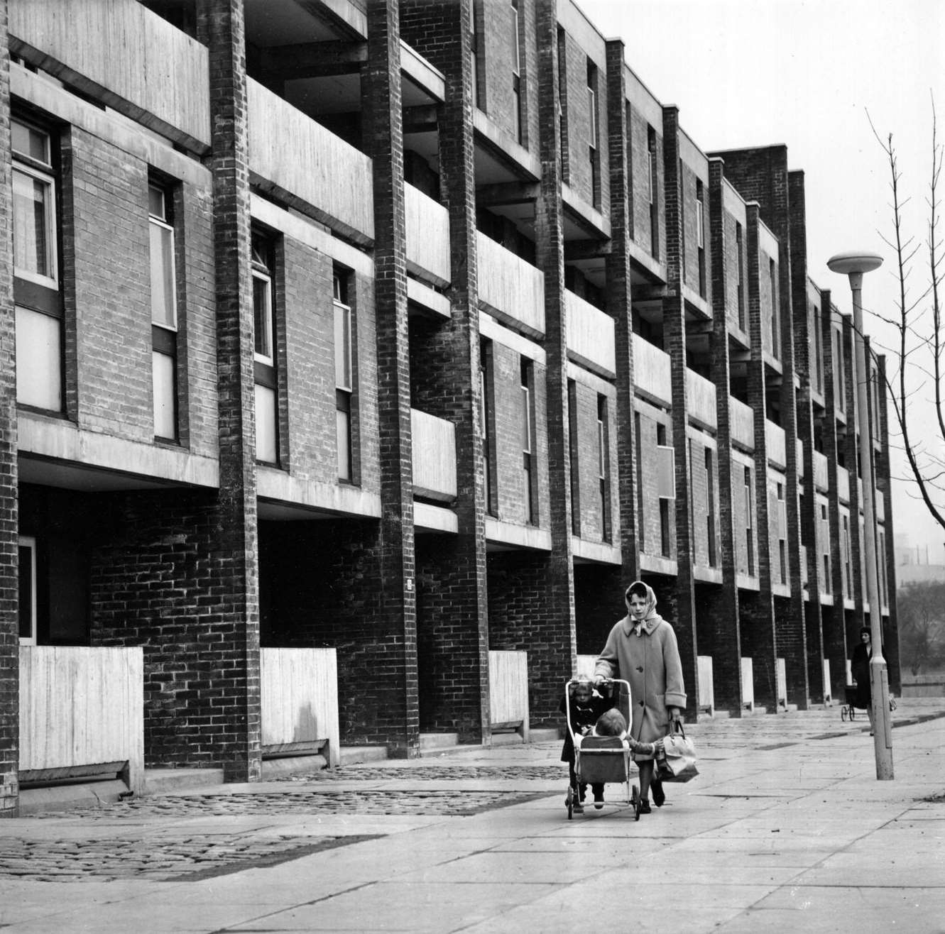 #103 A woman walking past a block of modern housing with two young children in the Gorbals area of Glasgow, 1960