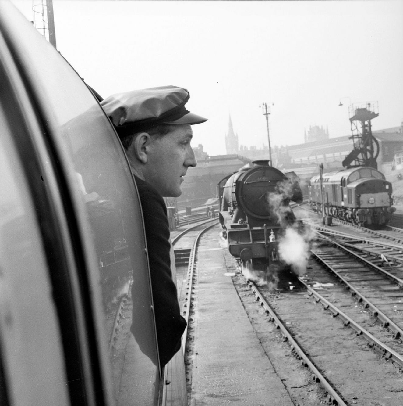 #149 The railway employee responsible for the oiling on board the Flying Scotsman looks at an old steam locomotive in a siding at King’s Cross Station in London as the train leaves for Edinburgh on its centenary journey, 1962