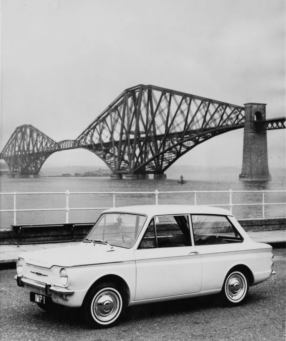 #34 The Scottish built Rootes Group Hillman Imp compact, rear-engined saloon car seen near the Forth Bridge cantilever railway bridge across the Firth of Forth on 3 May 1963 near Edinburgh, Scotland.