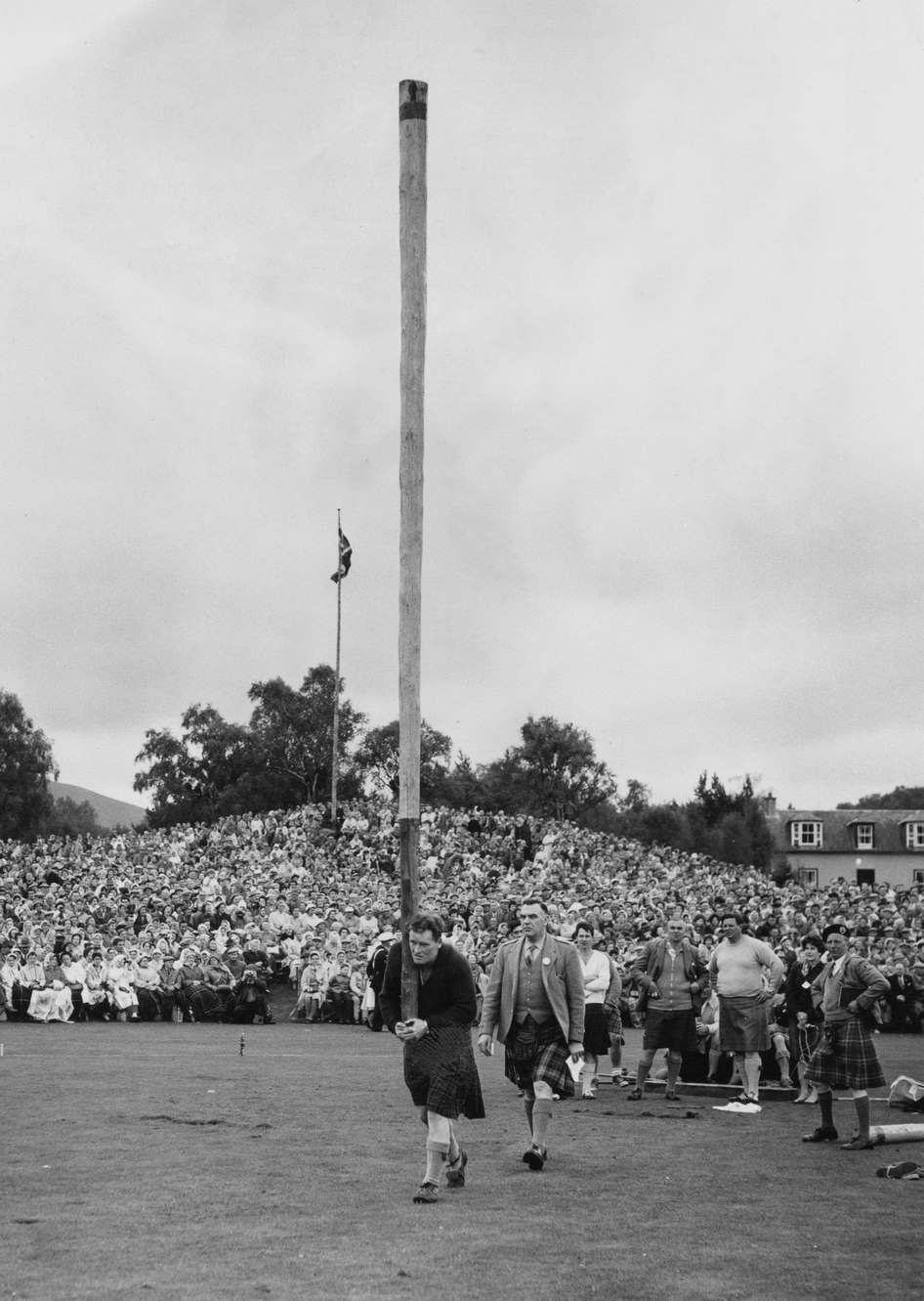 #57 British Highland Games athlete Bill Anderson watched by officials as he competes in the caber toss event of the Braemar Gathering in Braemar, Aberdeenshire, Scotland, 9th September 1961.