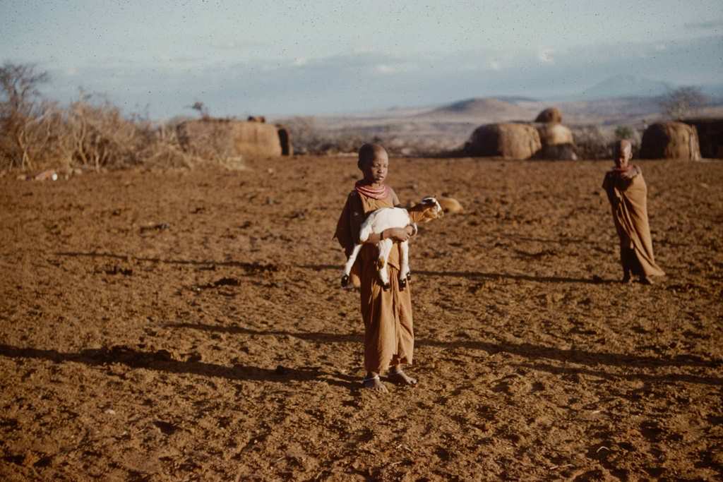 #29 A young boy as he holds a goat kid in his arms in a small village, Tanzania, 1962.