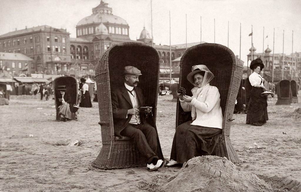 #34 A couple on holiday seated in beach chairs, she eating grapes and he smoking a cigar at the seaside in Scheveningen near The Hague in the Netherlands, 1910.