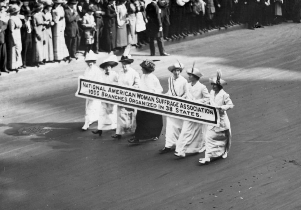 #14 Members of the National American Woman Suffrage Association marching with a banner which publicises their ‘1000 branches organized in 38 states’ at the New York Suffragette Parade.