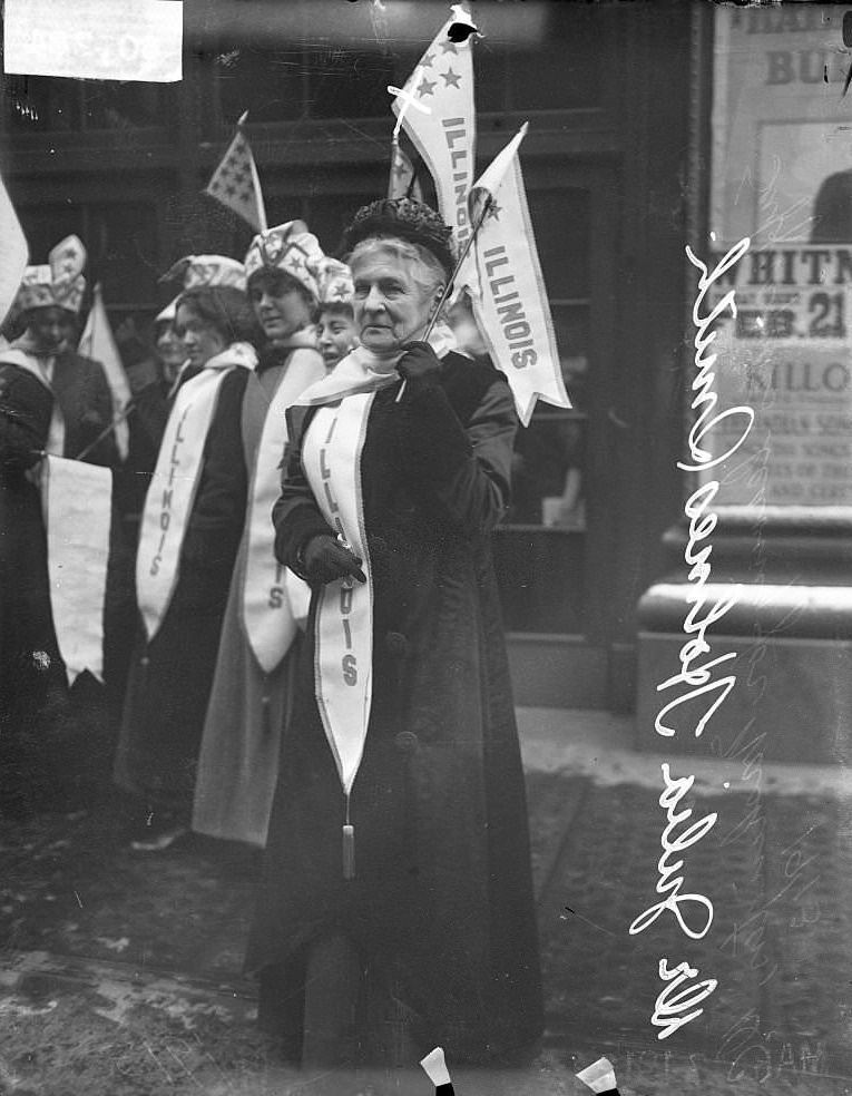 #22 Suffragette Dr Julia Holmes Smith, wearing a banner and holding a flag, demonstrating with other suffragists in Chicago, Illinois, February 27, 1913.