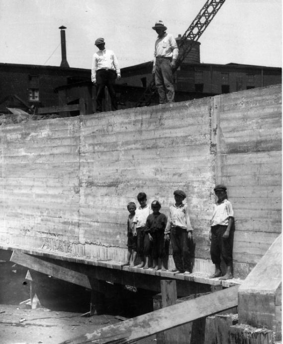 #79 Five boys standing along the base of a poured concrete wall at a construction site, 1902