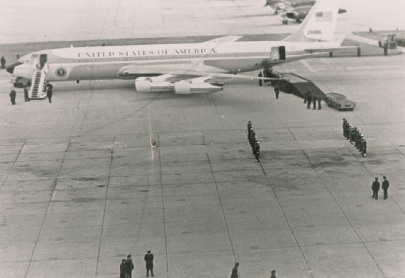 #24 Air Force One carrying the casket of President Lyndon B. Johnson. People stand on the tarmac, some at attention, 1973