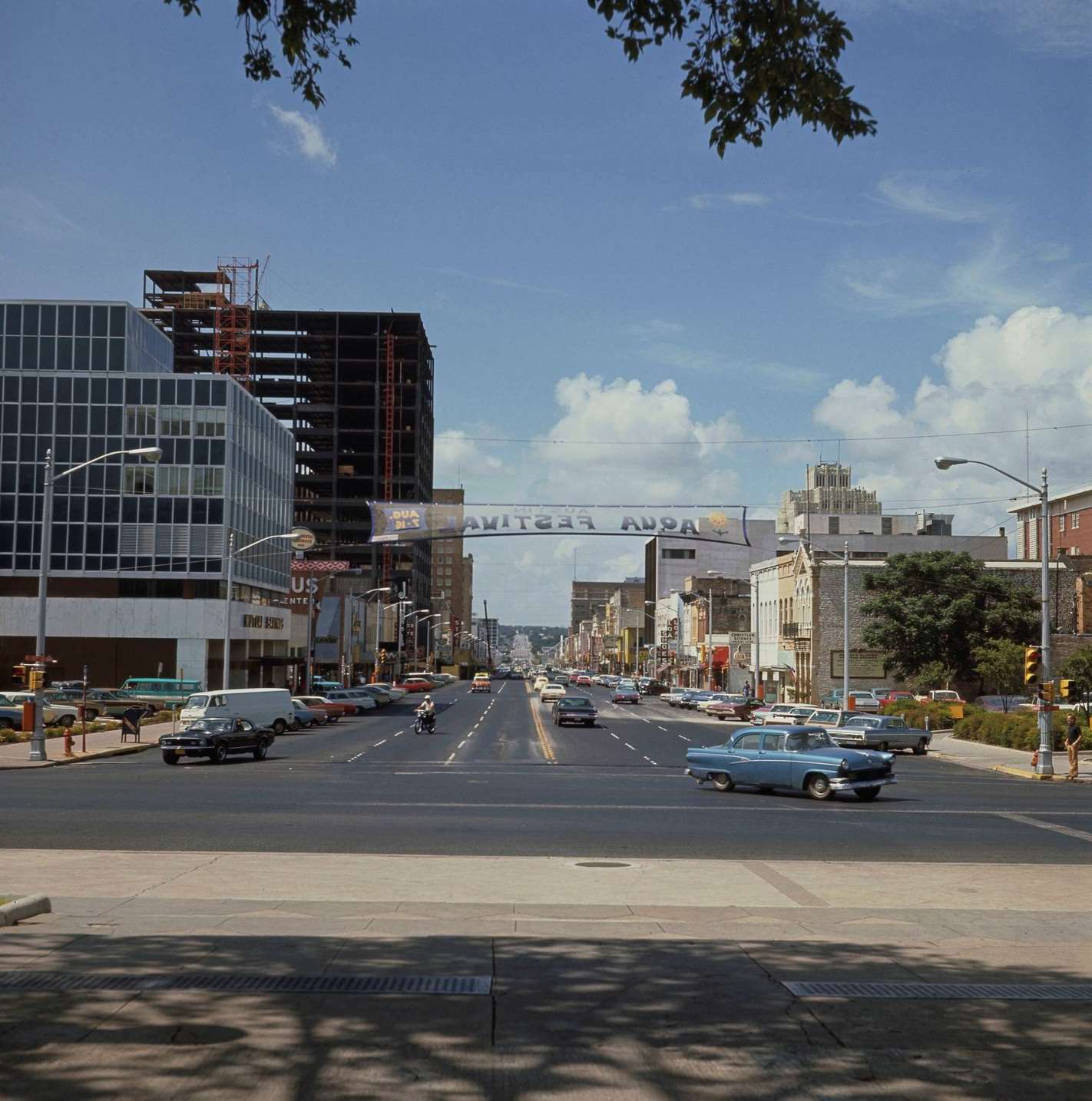 #18 Cars drive up and down Congress Avenue at the intersection with 11th Street in the downtown district of the city of Austin, 1970