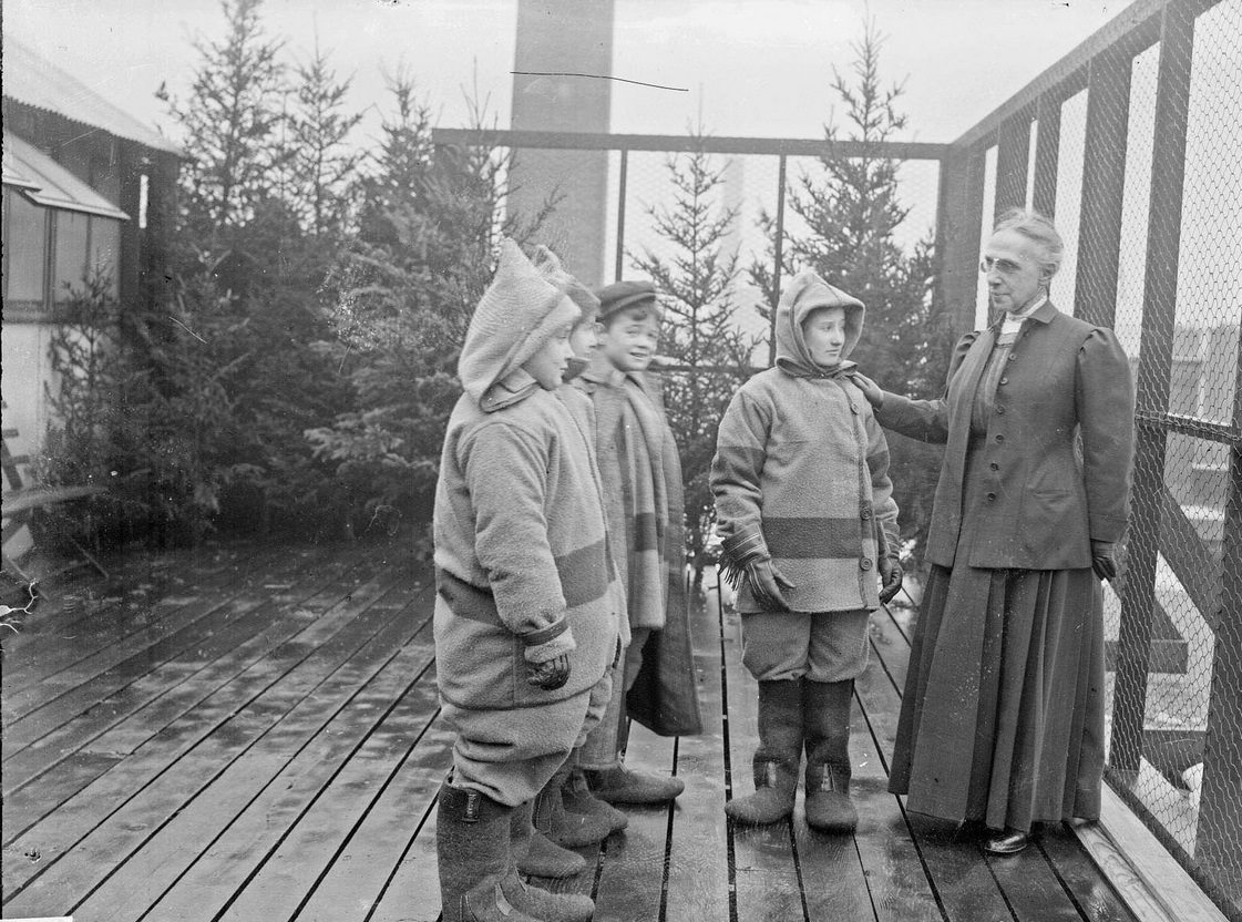 #153 Superintendent of schools Mrs Ella Flagg Young standing with students outdoors at the Mary Crane Nursery, an open-air school, located at 782 West Cabrini Street (formerly 782 Ewing), Chicago, Illinois, 1910s.
