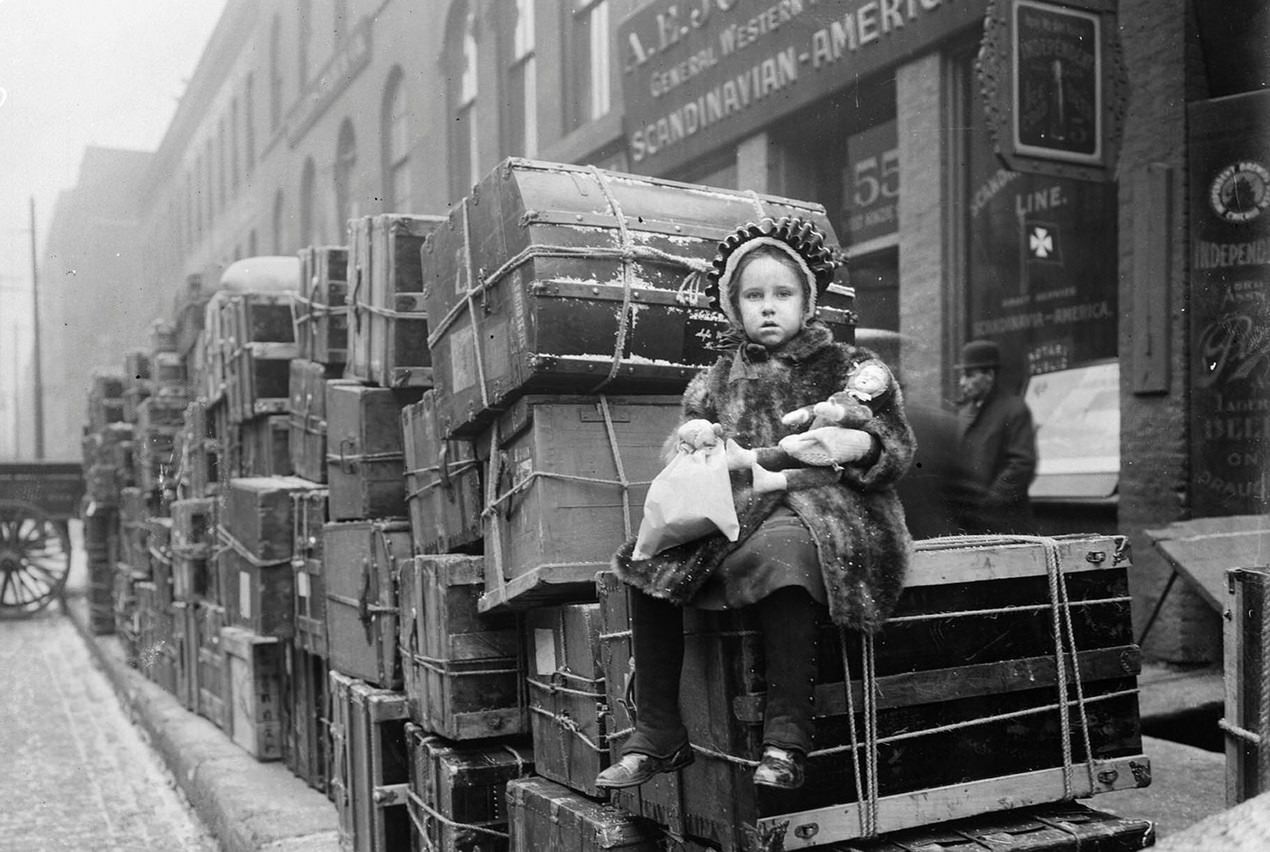 #161 Girl sitting on stacked trunks belonging to Norwegians going home to Norway, Chicago, Illinois, 1910s.