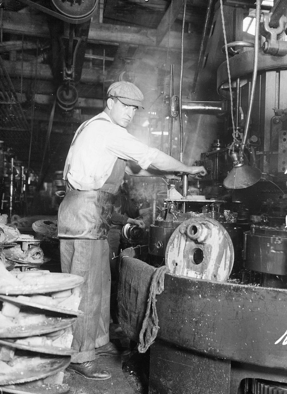 #57 Baseball player Jim Vaughn, of the National League’s Chicago Cubs, wearing street clothes and holding on to a lever attached to a large piece of machinery, standing in a room filled with machinery in or near Chicago, Illinois, 1918.