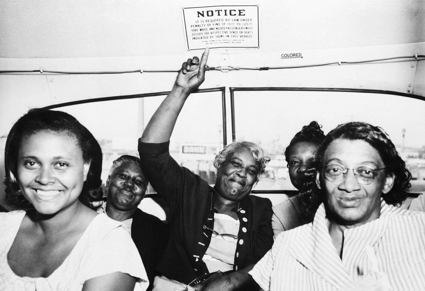 #1 A passenger points to one of the segregation signs removed from all Dallas Transit Company buses, following a Supreme Court ruling banning segregation on all public transportation within a state, 25th April 1956.