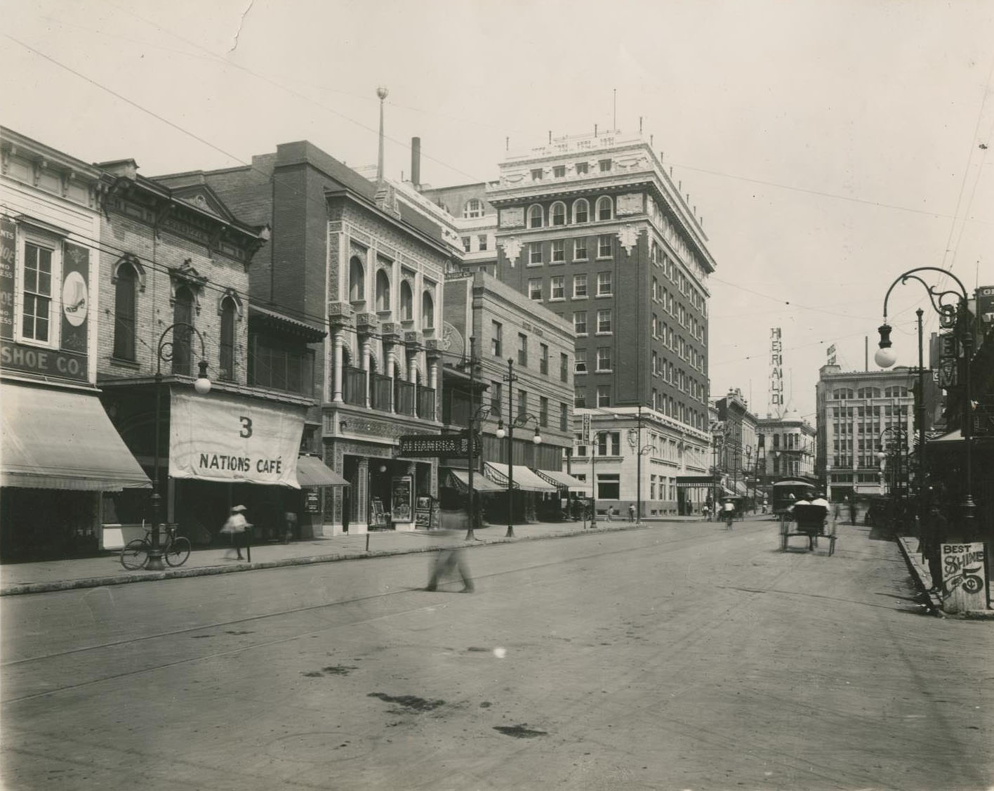 #65 A street in El Paso with various stores seen on the side to the left and a sign for the “Herald” seen in the background, 1900s