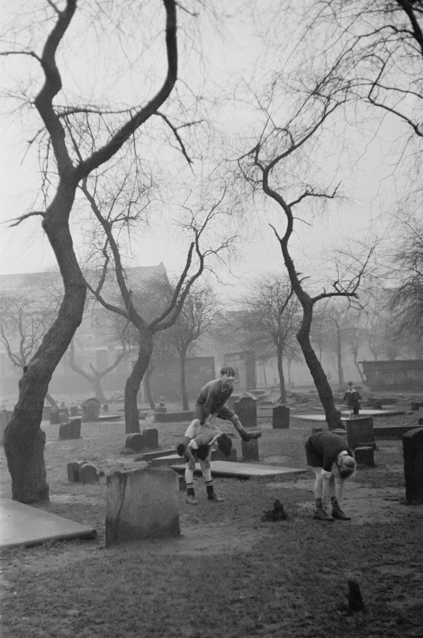 #50 A group of boys playing leapfrog amongst the gravestones of the Corporation Burial Ground in Rutherglen Road, one of the few areas of greenery in the Gorbals, a slum district of Glasgow, 1948.