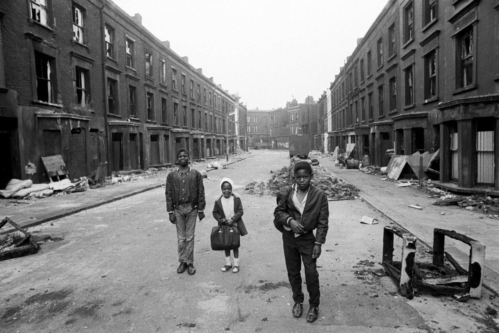 #87 Three children, including a little girl carrying a satchel, walking along a street of slum housing in the notorious Gorbals district of Glasgow in 1969.