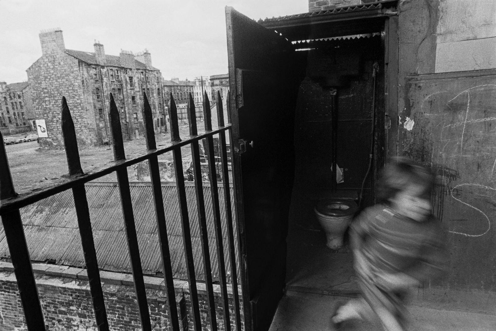 #59 A little boy leaving an outdoor toilet in slum housing in the notorious Gorbals district of Glasgow in 1969.