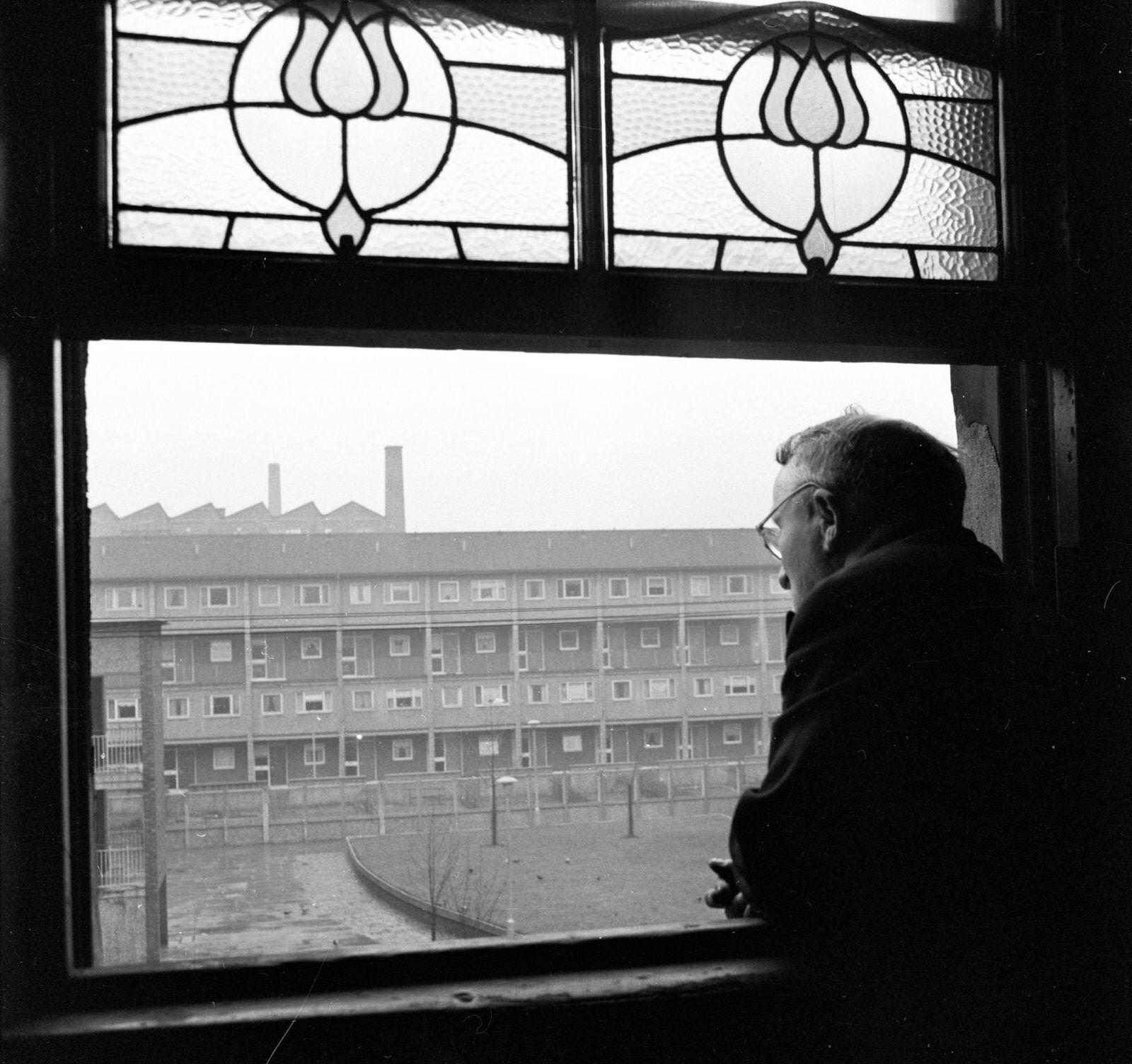 #75 A resident of the Gorbals area of Glasgow looking out of his window at a row of newly-built housing, 1962