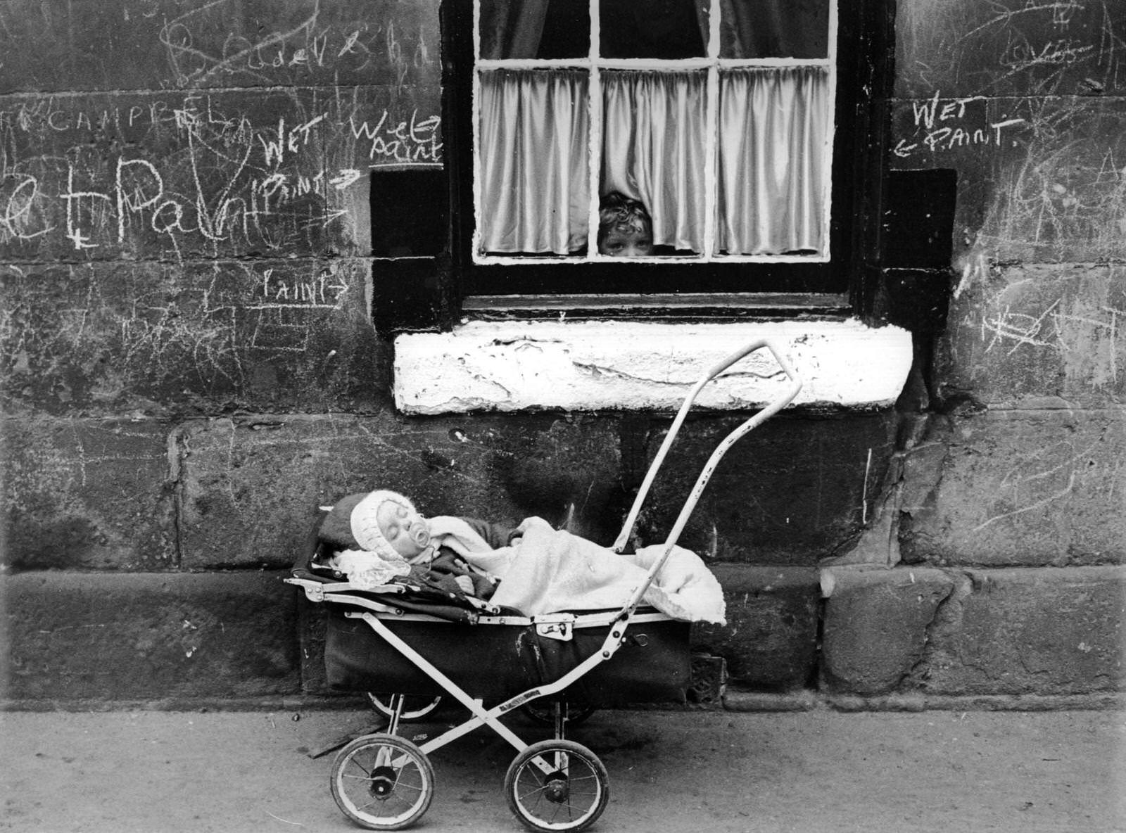 #83 A child looks at a baby in a pram from the window of a tenement block in the Gorbals area of Glasgow, before demolition, 1960