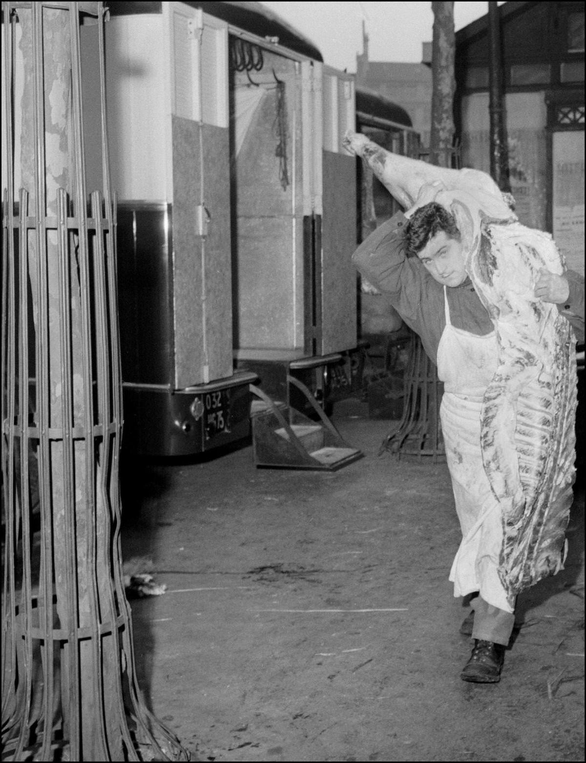 #69 An employee working for a butcher’s at the market of the Halles in Paris, carries in 1950s a part of beef.