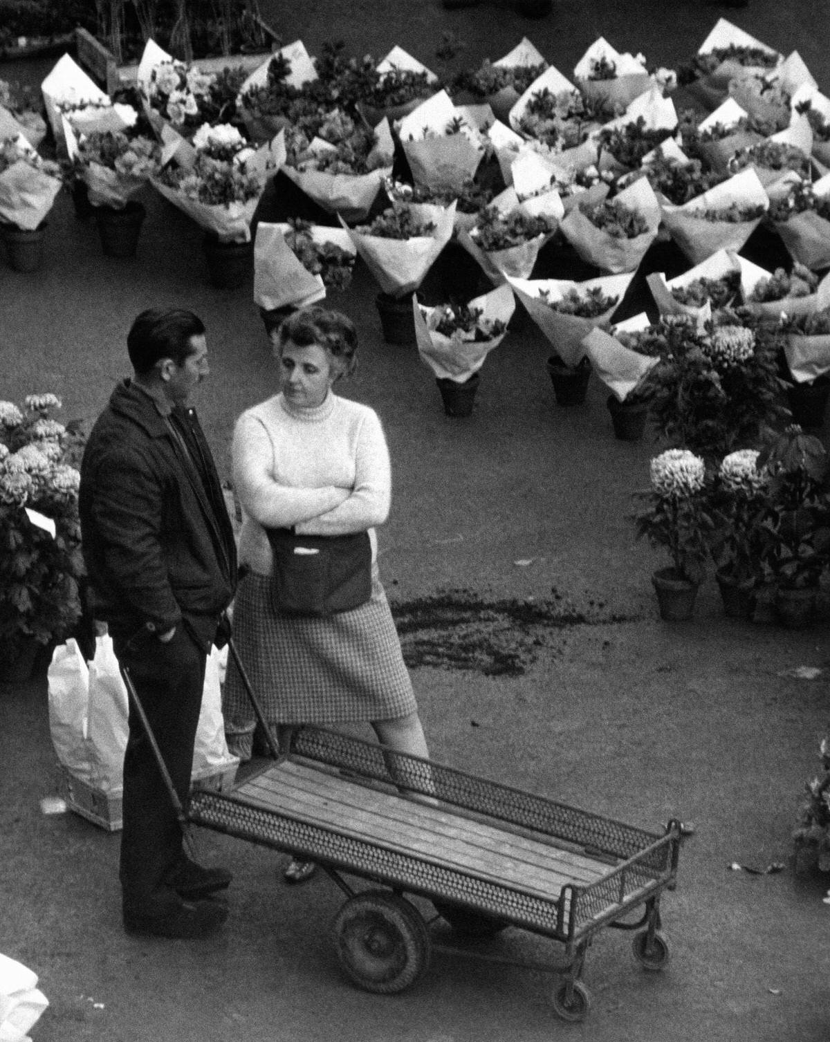 #109 A woman and a man speaking surrounded by bunches of flowers in Les Halles, 1967