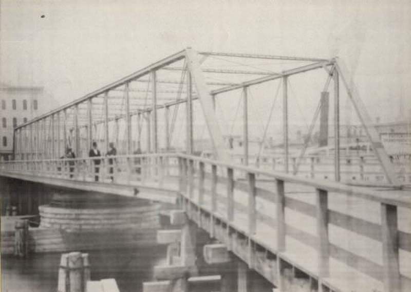 #23 Metal bridge over river with three men standing near the railing, 1870