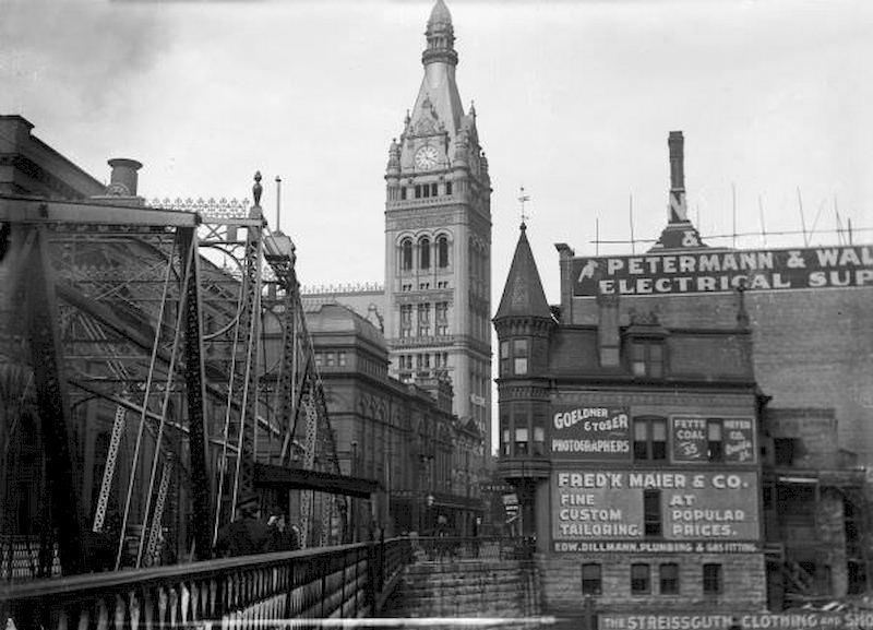 #18 A bridge crosses the Milwaukee River on Oneida Street, now known as Wells Street, looking toward the City Hall tower, 1895