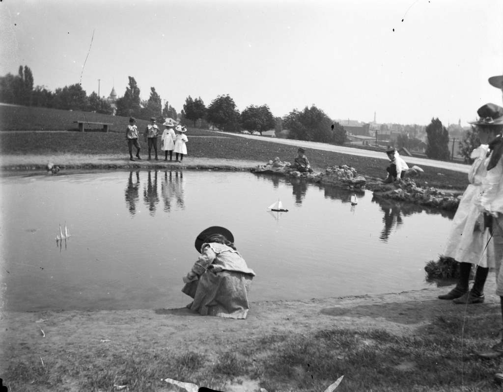 #113 Syl playing with toy boats at a small pond at Reservoir Park, Milwaukee, Wisconsin, August 28, 1898.