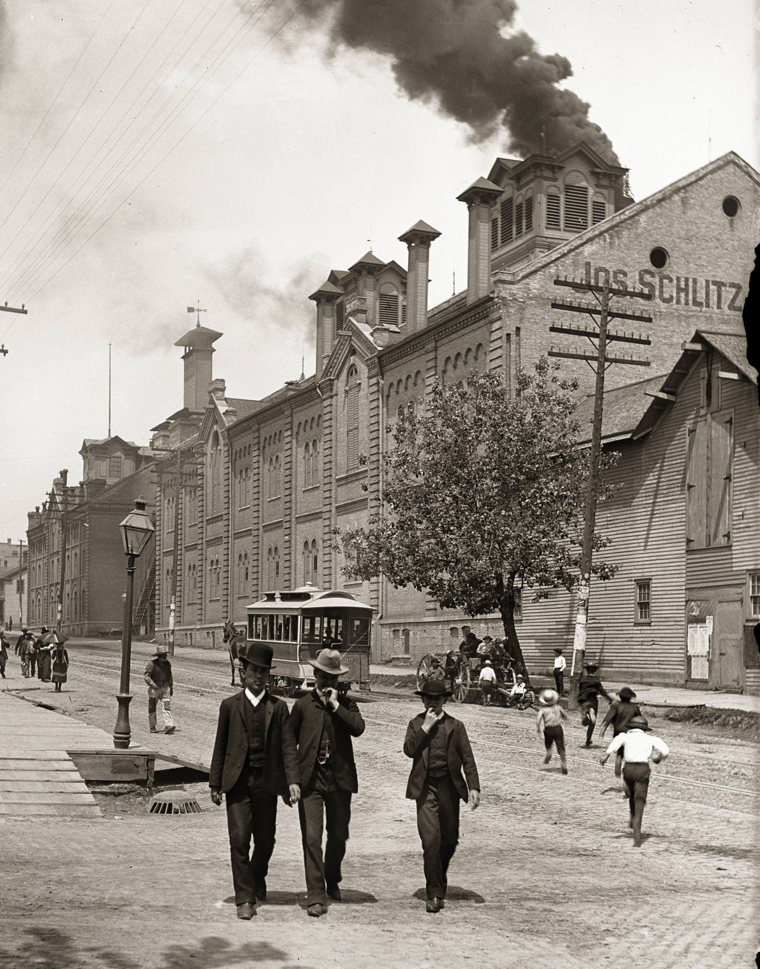 #27 Exterior of Schlitz Brewing Company with two men and a boy in suits and hats in the foreground, Milwaukee, Wisconsin, 1888.