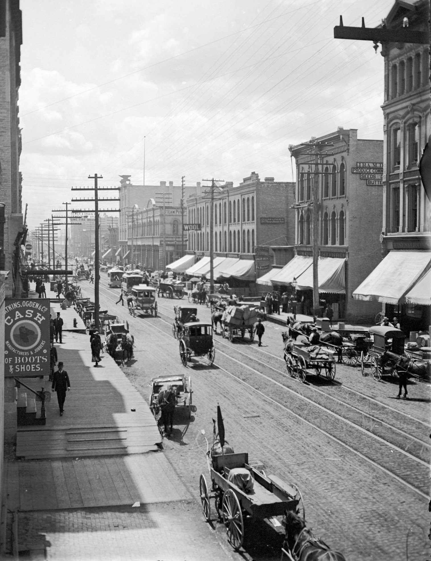 #71 Elevated view of West Water Street from Grand Avenue of horse-drawn vehicles, pedestrians, buildings, storefronts and power lines, Milwaukee, Wisconsin, 1885.