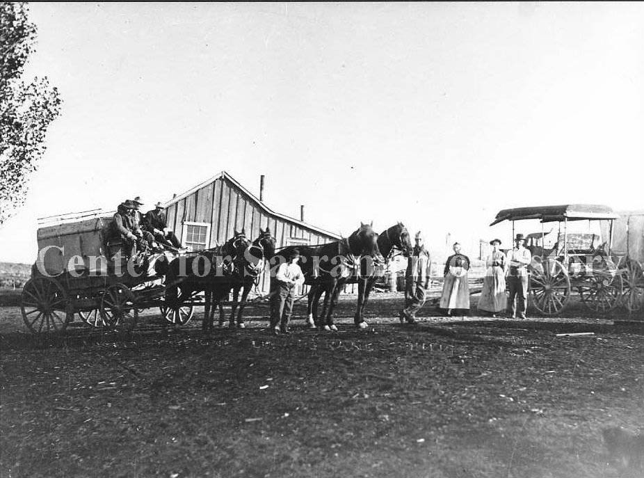 #142 Two stage coaches, one hitched with four horses, one parked and two women and three men standing next to the coaches, 1881