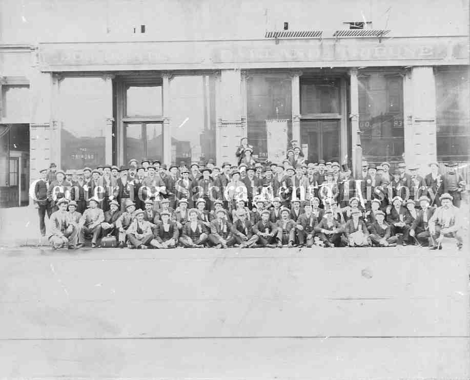 #17 acramento butchers gathered in front of Oakland Tribune building, posing with a banner, probably as part of a convention or meeting, 1885