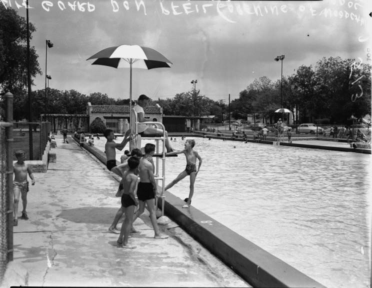 #56 Life Guard Don Pfeil sitting in how tower while being surrounded by children at Woodlawn Pool, 1954