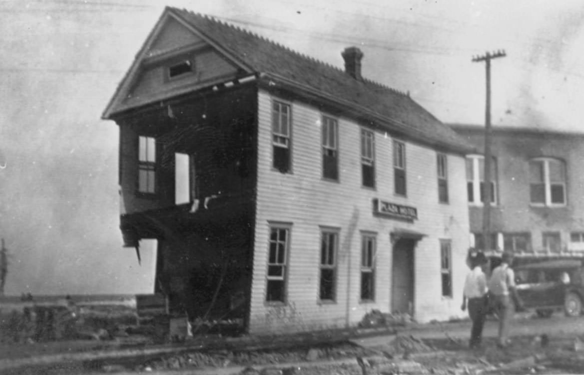#49 Plaza Hotel with one side of the lower level missing. Two men are walking past the building.