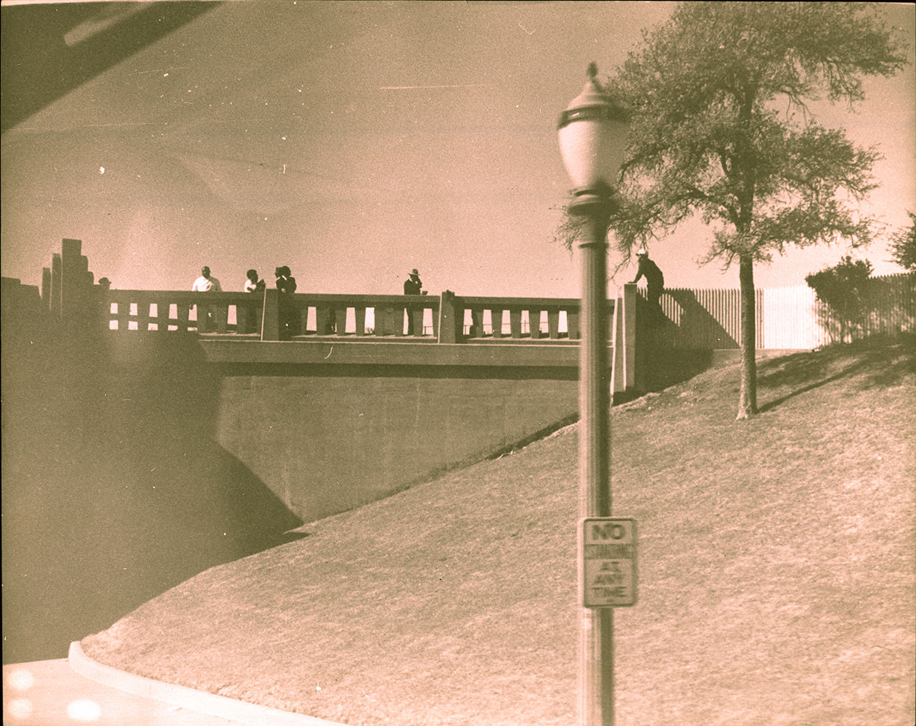 #128 People standing on bridge overlooking grassy knoll, 1963