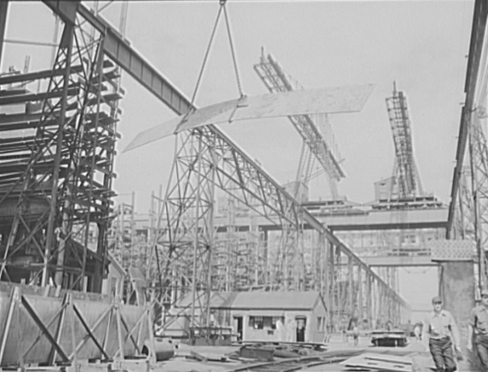 #31 A huge overhead crane swings this metal plate into position to be welded to a new cruiser under construction for the U.S. Navy, 1941