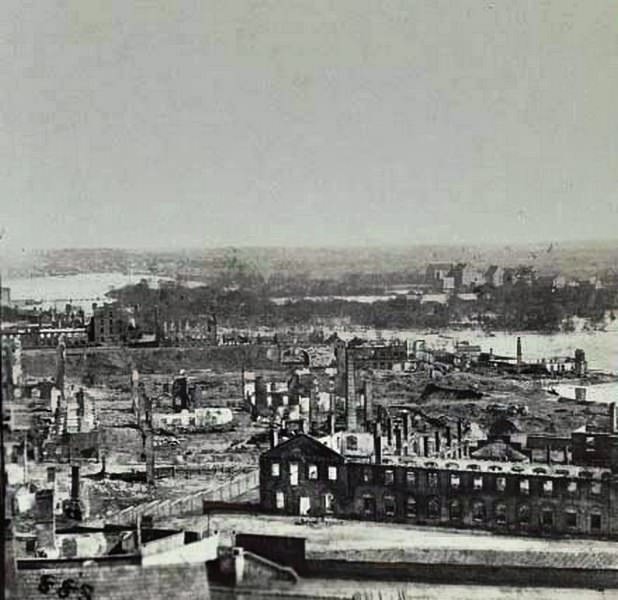 #127 An aerial view of the “burnt district” in Richmond, taken from the old arsenal. The James River in background, 1865