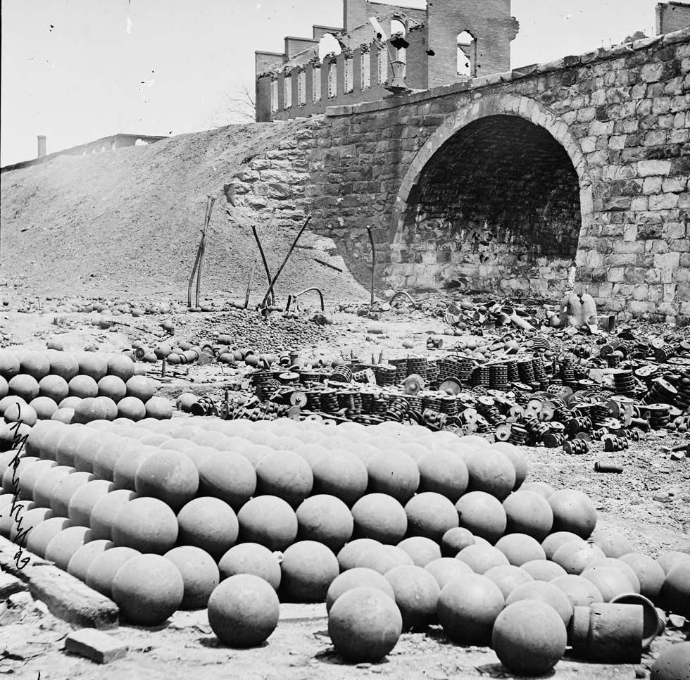 #182 Piles of solid shot, canister, etc., in the Arsenal grounds; Richmond & Petersburg Railroad bridge at right, 1864