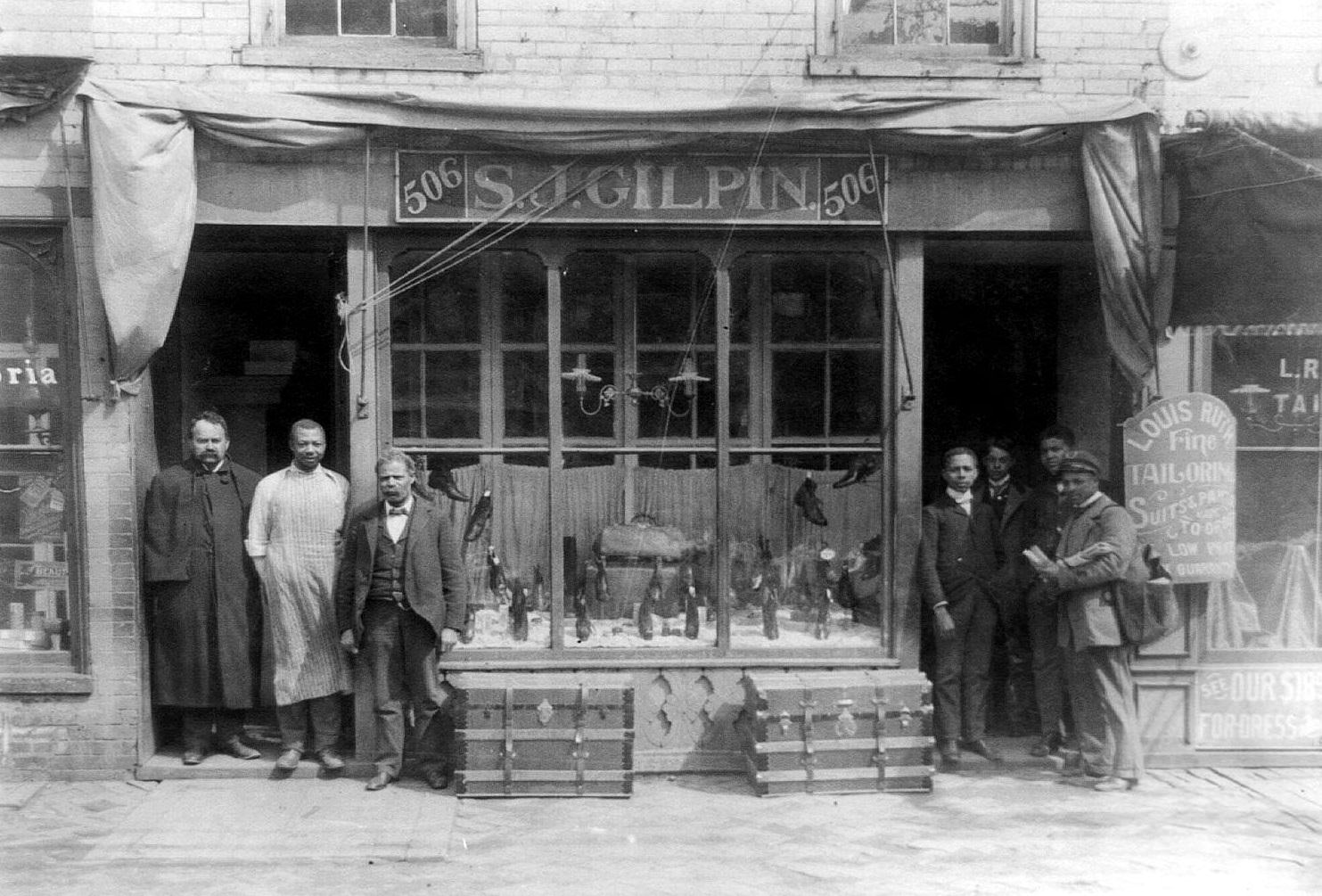 #49 Mail carrier and six other men posed standing at entrance to shop. S.J. Gilpin shoe store, Richmond, 1900