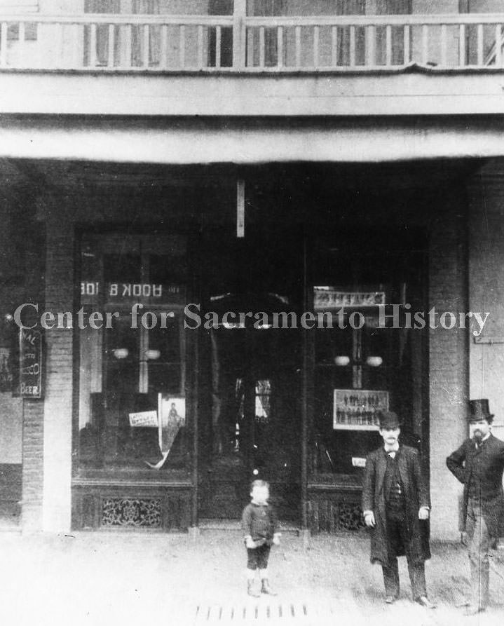 #37 Store front on J Street with a men and a small boy posing in front of the store, 1868