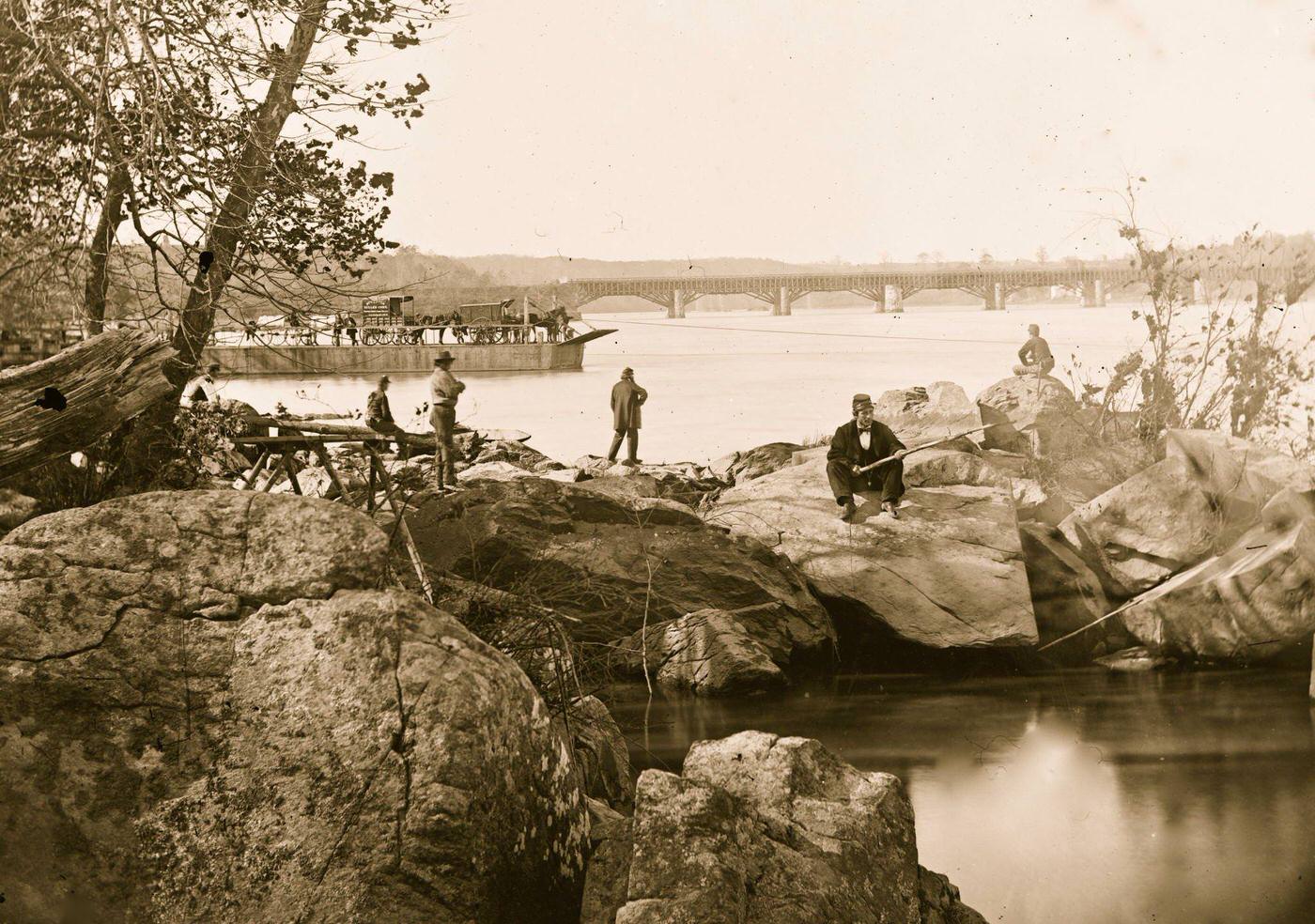 #43 Georgetown ferry-boat carrying wagons, and Aqueduct Bridge beyond, from rocks on Mason’s Island, 1863
