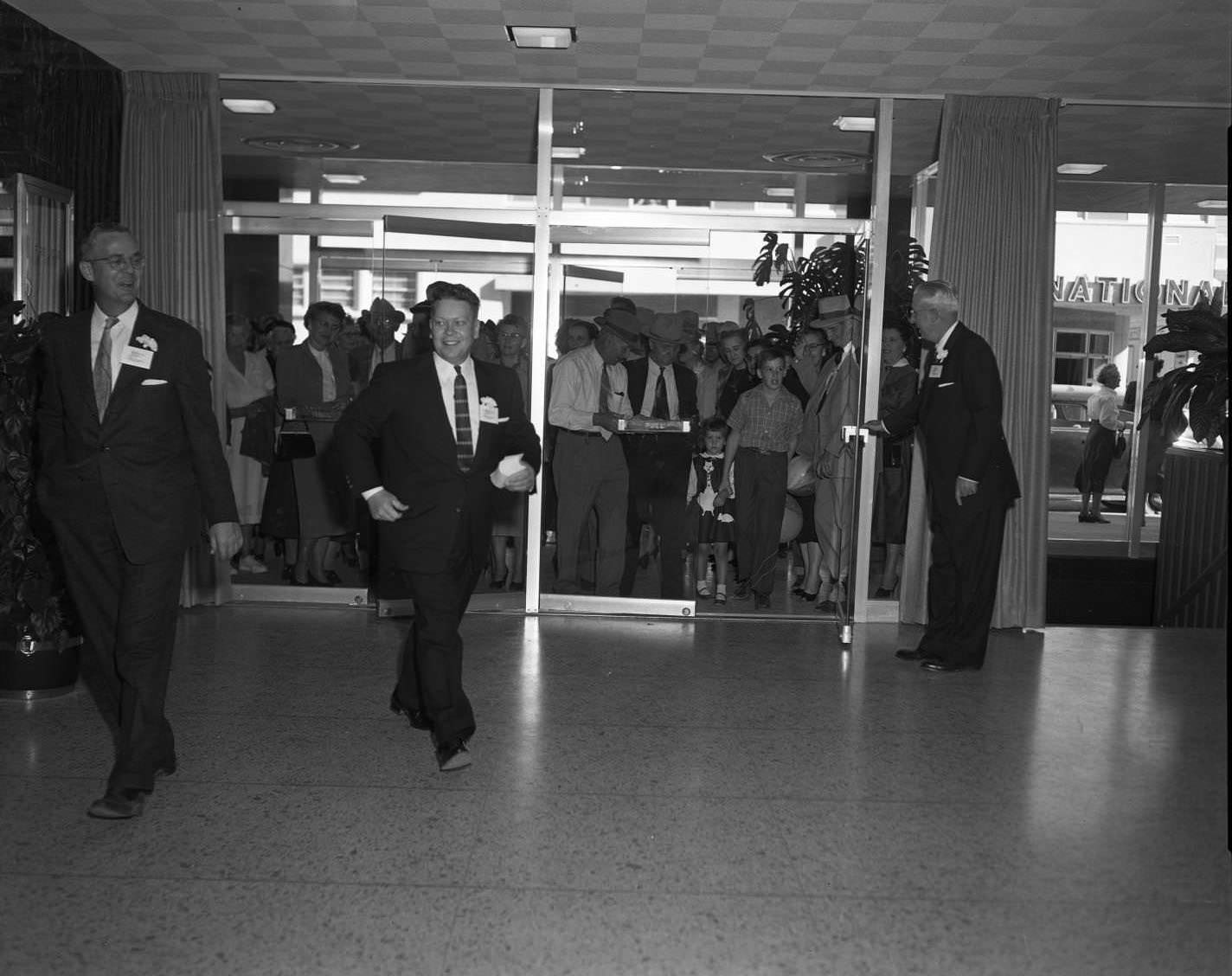 #142 A large group of people behind the two sets of glass double doors inside of the Citizens National Bank, 1956