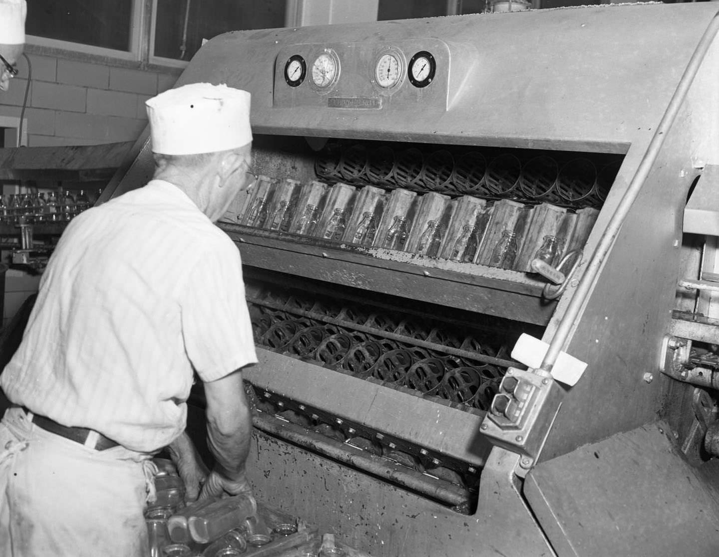 #19 A machine at a dairy in Abilene, 1958. Fourteenth and Butternut Streets. A worker is putting glass bottles into the machine.