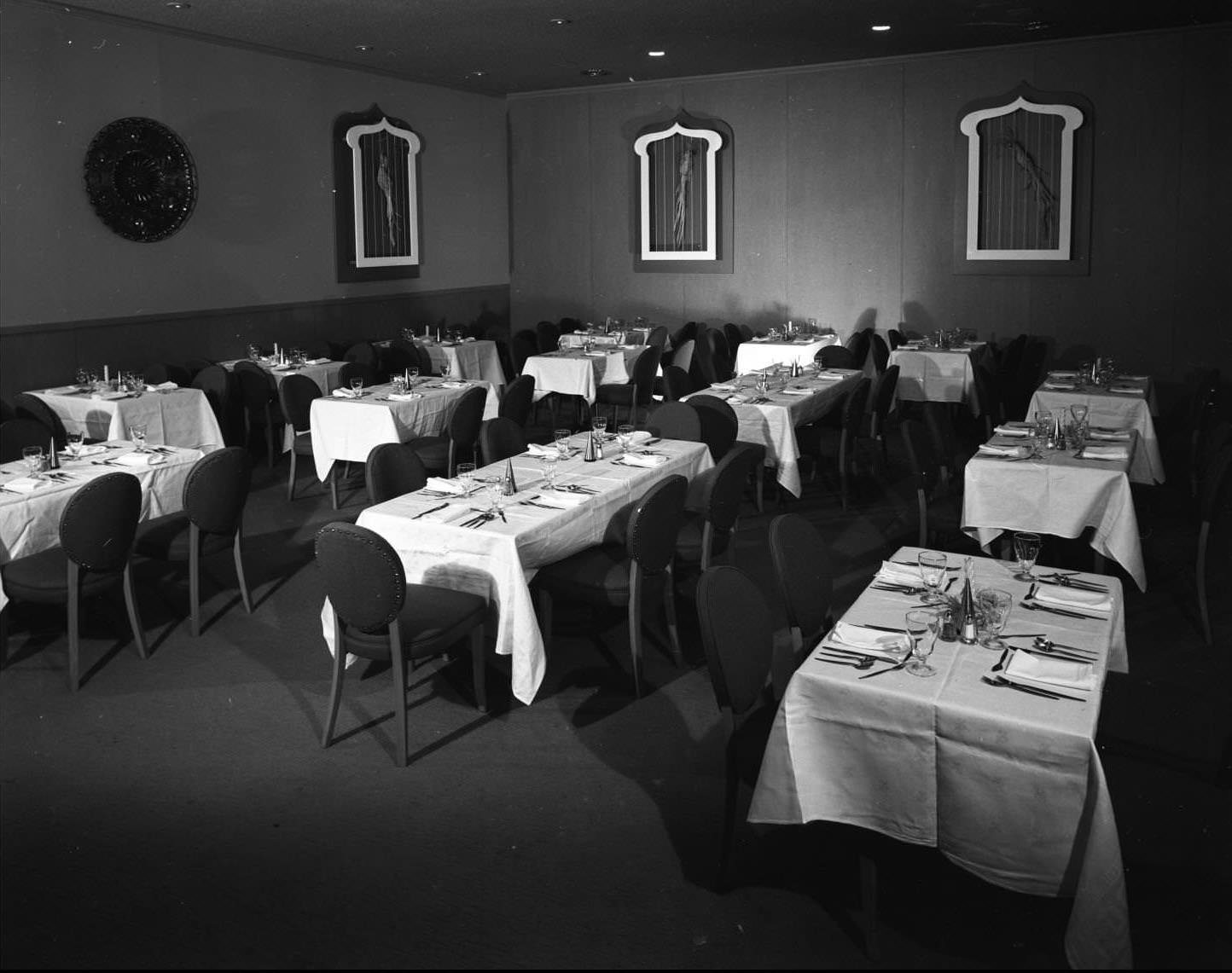 #25 Paradise Room restaurant in the Sands Hotel, 1956. There are tables set for four or five people. There appears to be pictures of birds along the walls.