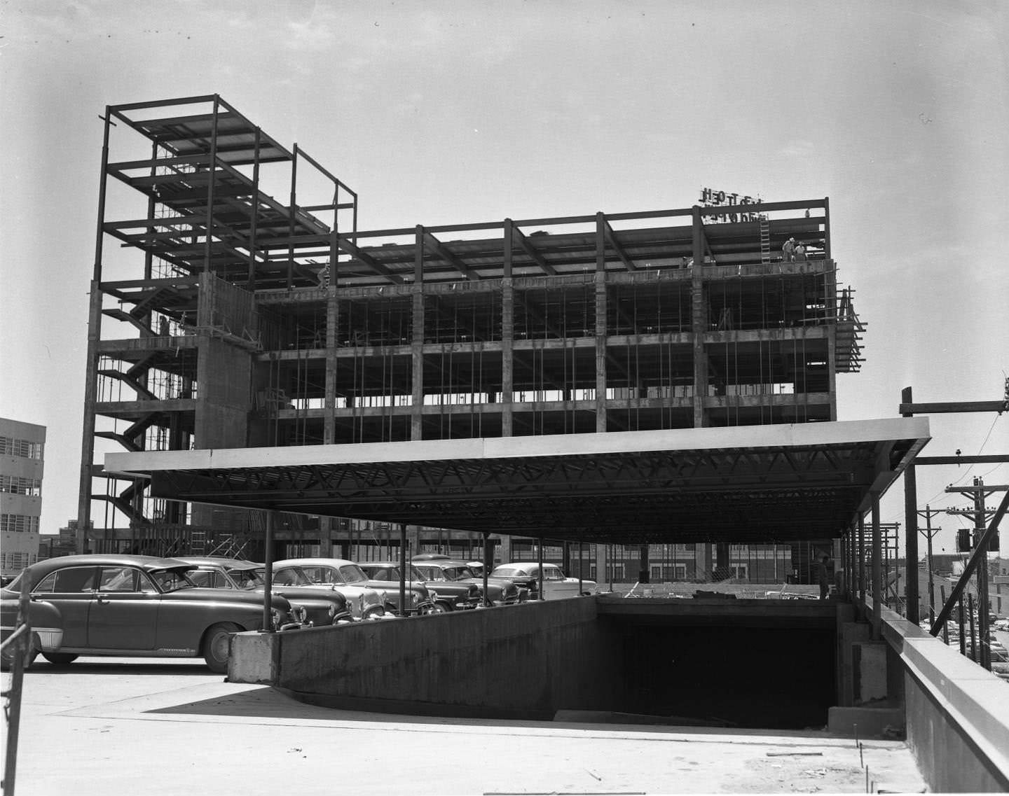 #8 The Citizens National Bank under construction, 1954. The multi-story building’s frame is partially completed. There are men working and cars parked at the site.