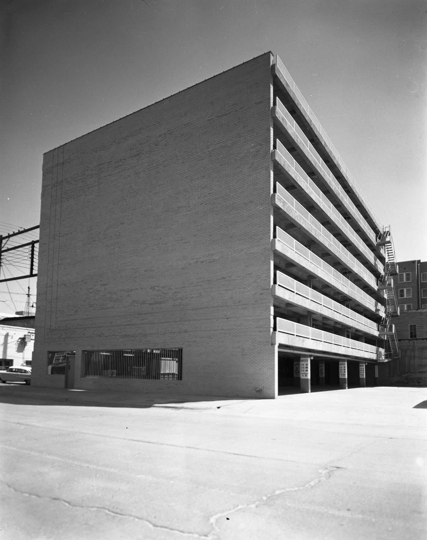 #99 Parking garage at F and M Bank, 1955. The building has seven above ground levels. There are buildings, a car, and power lines behind it.