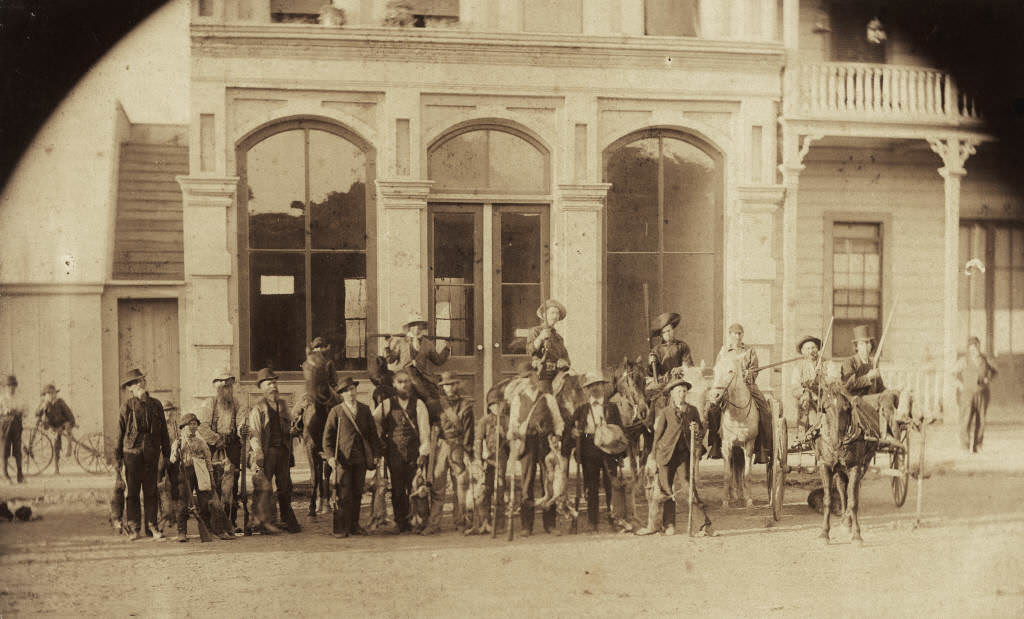#109 Rabbit hunting party standing in front of three large glass windows of the barber shop owned by Frank Ey on West Center Street (now Lincoln Ave.), Anaheim, 1893