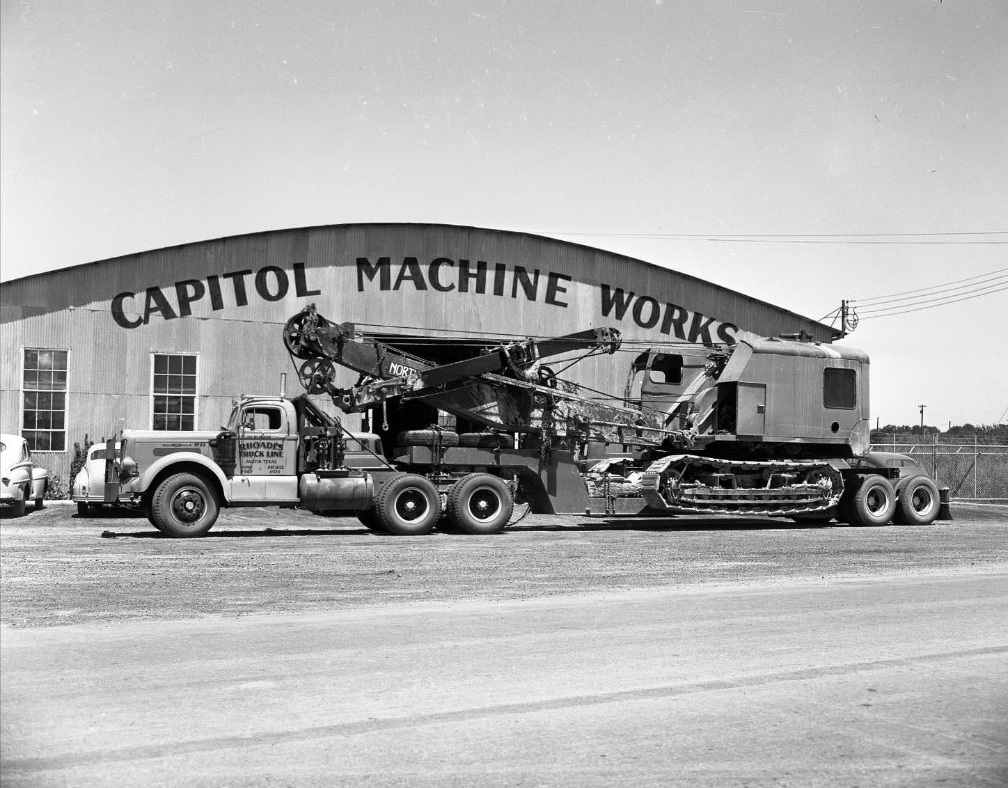 #189 Flatbed truck loaded with crane parked in front of Capitol Machine Works building, on 4824 East 1st Street in Austin, 1951